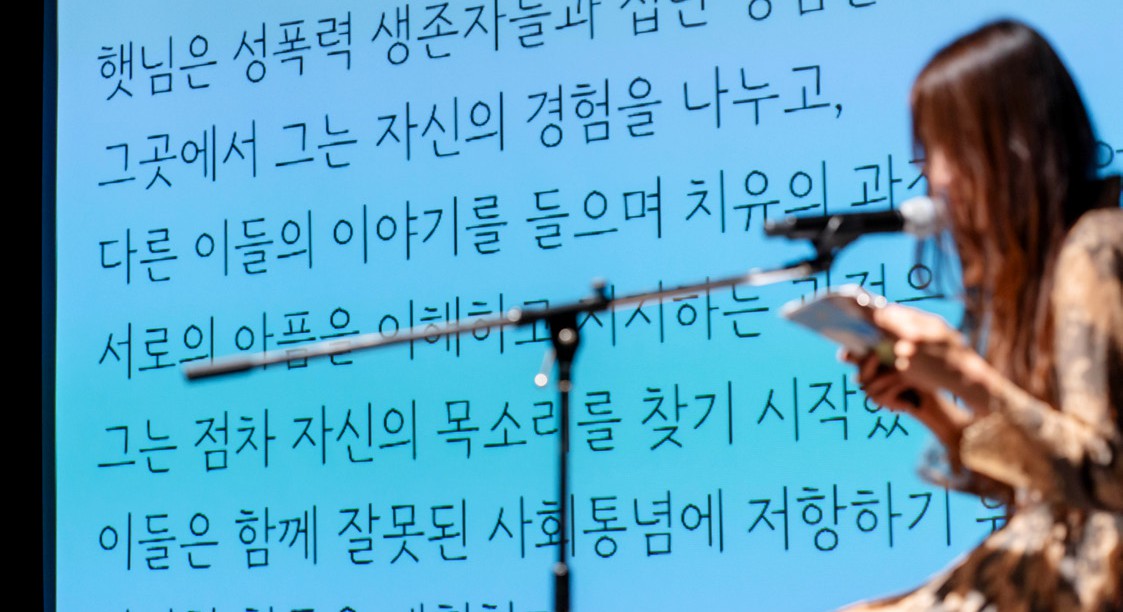 세 번째 이끔이 햇님이 무대에서 자신의 경험을 나누는 자료집의 글이 스크린에 비친 가운데 발화하는 모습